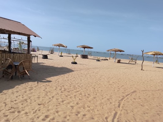 The bar and cane chairs beside the wide sandy beach at Gunjur, with parasols and fishing boats out on the water.